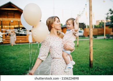 Mom Holds A Baby In Her Arms And Air Balloons. Birthday Party