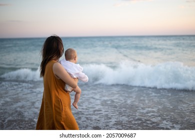 Mom holds her son in her arms. Mother and the child meets the sunset on the sea. pastime of mom and son. Happy motherhood. Mom and son relationship.