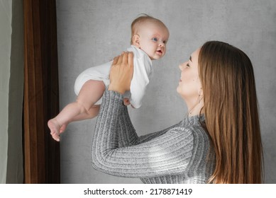 Mom Holds A Infant Baby In Her Arms Close-up. Loving Mother Carrying Of Her Newborn Baby At Home. Bright Portrait Of Happy Mum Holding Cute Infant Child An Arm's Length Hands.