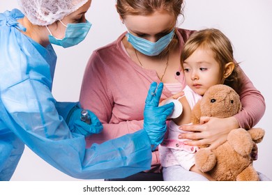 Mom Holds Kid In Her Arms And Calms Down After Vaccination. The Doctor Puts A Cotton Pad On The Injection Site. White Background.