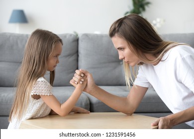 Mom And Kid Daughter Arm Wrestling Having Fight Confrontation Or Family Conflict, Mother In Law And Stubborn Child Girl Holding Hands Competing With Serious Focused Faces Expressing Disagreement