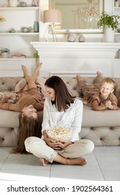 Mom And Kids Eat Popcorn At Home On A Day Off. A Woman A Boy And A Girl Relax On The Couch And Hug