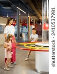Mom with kids learn physics interactively on a model that shows physical phenomena while visiting a science museum. Concept of children