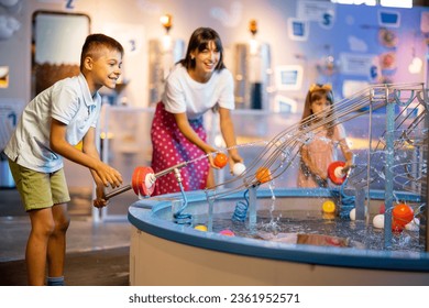 Mom with kids play with balls, learning physical phenomena in an interesting way, having fun in a science museum with interactive models