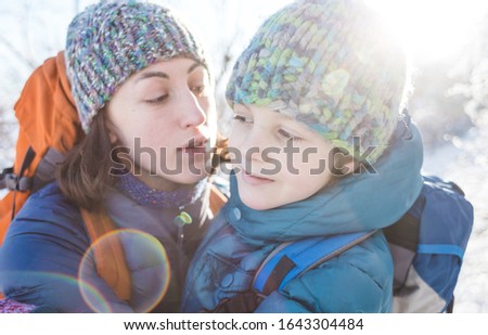 Mom kisses and hugs her son. A woman walks with a child in a winter park. The boy spends time with his mother. Mother's love. Walk through the snowy forest. Family portrait.