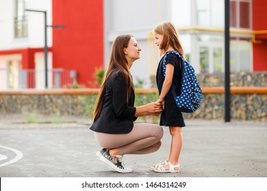 Mom Leads Her Daughter To School. Return To School. Woman And Girl With Backpack Behind The Back. Beginning Of Lessons. First Day Of Fall.