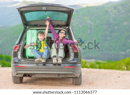 Mom and little boy sitting in hatchback car with mountain background
