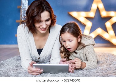 Mom And Little Daughter Lying On The Floor And Playing Tablet