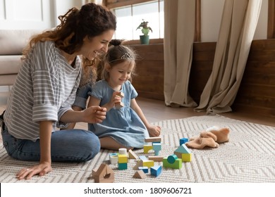 Mom And Little Daughter Play With Color Wooden Bricks Toys Set. Baby Sitter And Small Kid Girl Sit On Warm Floor On Carpet Enjoy Funny Game Together. Educational Activity, Development Of Child Concept