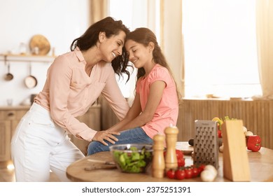 Mom and little daughter sharing heartfelt moment touching foreheads while preparing a healthy salad, cherishing family love and bonding during dinner preparation in kitchen at home - Powered by Shutterstock