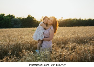 Mom and little daughter in summer dresses standing on the ripe wheat field and hug. A mother holding in his arms cute child in a wheat field. Happy family travels. Happy childhood. - Powered by Shutterstock