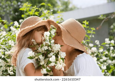 mom and little daughter wearing straw hats embrace amid flowering jasmine bushes in garden in summer. Aromatherapy and Spa concept. natural eco product. stress relief - Powered by Shutterstock