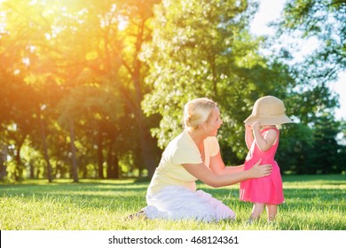 Mom And Little Girl Playing Peek A Boo With A Big Hat In The Sunset Park.Lens Flare, Copy Space