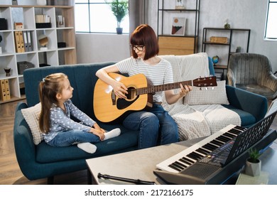 Mom And Little Happy Girl In Music Therapy By Playing Guitar On Music Room. Teacher Helping Young Female Pupil In Guitar Lesson. Relaxing At Home.