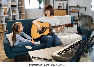 Mom And Little Happy Girl In Music Therapy By Playing Guitar On Music Room. Teacher Helping Young Female Pupil In Guitar Lesson. Relaxing At Home.