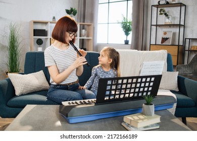 Mom and little happy girl in music therapy by playing flute on music room. Teacher helping young female pupil in flute lesson. Relaxing at home. - Powered by Shutterstock