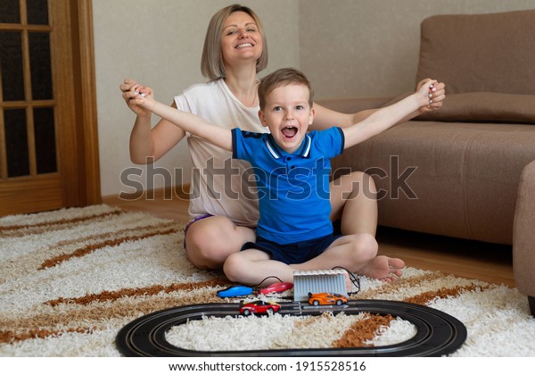 Mom and little son play racing on the carpet at\
home, have fun and cuddle.