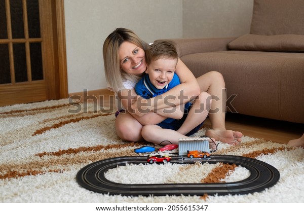 Mom and little son play racing on the carpet at\
home, have fun and cuddle.