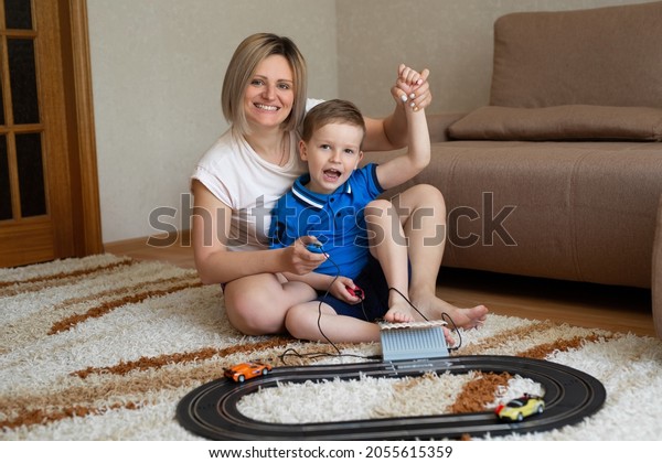 Mom and\
little son play racing on the carpet at\
home.