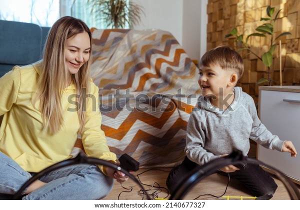 Mom and\
little son play racing on the carpet at home, have fun and hug.\
Single mother raises her son by playing\
cars