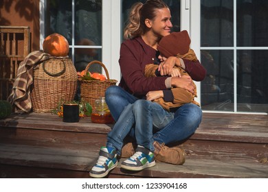 Mom and little son are sitting on the porch hugging on a warm autumn Sunny day. Pumpkins, sea buckthorn in wicker baskets on the porch of a country house with autumn leaves and tea in the teapot.  - Powered by Shutterstock