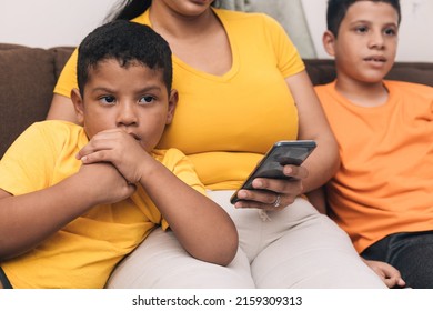 Mom Looking At The Cell Phone, Sitting With Her Two Children In The Armchair