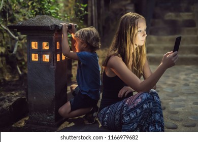 Mom looks into her smartphone, the son looks into the luminous cozy window of the house. The boy lacks Attention, care, love and home comfort