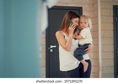 Mom Makes A Phone Call With Dad. Holding A Baby In Her Arms. Busy Family Time. Home-friendly Clothing From The New Collection.