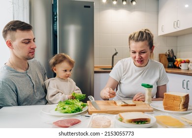 Mom Making A Sandwich With Salad, Ham And Cheese For Husbend And Little Doughter. American Cuisine. Fast Food. Cooking