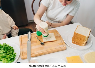 Mom Making A Sandwich With Salad, Ham And Cheese For Husbend And Little Doughter. American Cuisine. Fast Food. Cooking