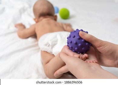 Mom massage the baby's feet with a purple rubber ball. Baby massage. Selective focus