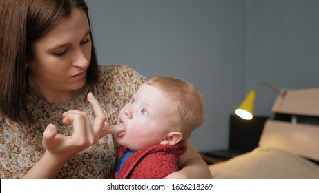 Mom Massages Baby Gums Using Toothbrush Massager Worn On Finger And Gum Gel. Teething Concept