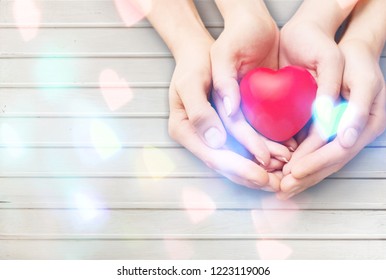 Mom Mother's Hand Holding Daughter, Son Child Kid Palm Supporting Red Heart Love Ball On Light White Wood Background: Nursing Children Home Day Care Health Care Concept: Hospital Medical Business