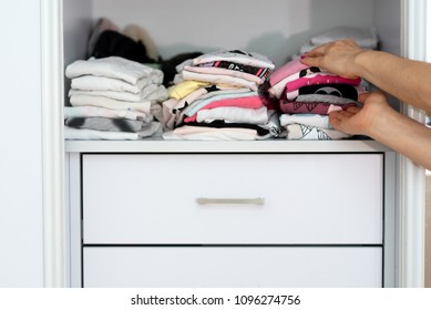 Mom Picking Out  Kid Outfit At Home To Send Her Children Back To School. New Colored Clothing Stacked In A Pile Close-up In White Closet. Woman Folding Clothes On A Shelf In A Closet.