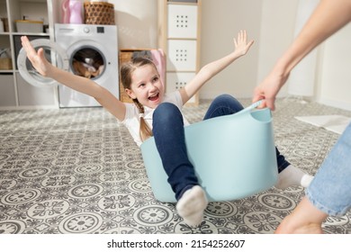 Mom is playing with daughter who is sitting in laundry bowl little girl wants to spend time with woman and help with household chores mother drags her daughter around laundry room for fun in bowl.