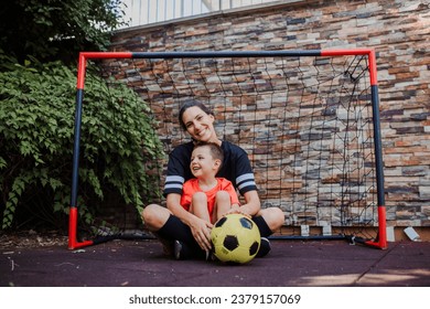 Mom playing football with her son, dressed in football jerseys. The family as one soccer team. Family sports activities outside in the backyard or on the street. - Powered by Shutterstock