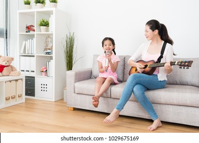 Mom Playing Guitar On The Sofa And Daughter Sing Songs Creatively With The Tunes.