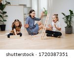 Mom playing with kids on the kitchen floor, helping his little son and daughter build tower from wooden blocks, but it collapses to their surprise and exhilaration.