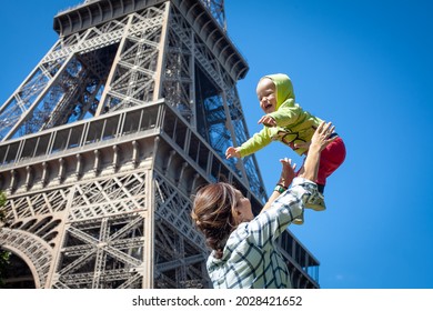 Mom Plays And Laughs With The Baby Against The Backdrop Of The Eiffel Tower. Blue Sky. The Kid Is Flying.