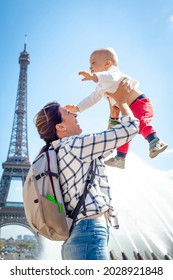 Mom Plays And Laughs With The Baby Against The Backdrop Of The Eiffel Tower. Blue Sky. The Kid Is Flying.