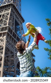 Mom Plays And Laughs With The Baby Against The Backdrop Of The Eiffel Tower. Blue Sky. The Kid Is Flying.