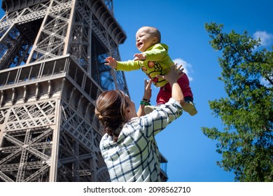 Mom Plays And Laughs With The Baby Against The Backdrop Of The Eiffel Tower. Blue Sky. The Kid Is Flying.