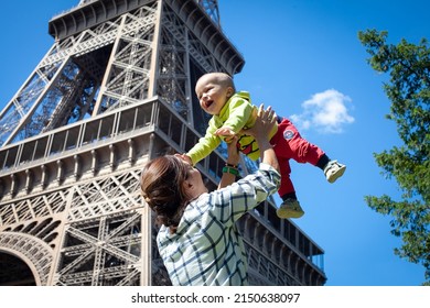 Mom Plays And Laughs With The Baby Against The Backdrop Of The Eiffel Tower. Blue Sky. The Kid Is Flying.