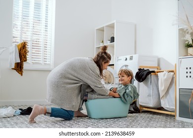 Mom plays with son who sits in laundry bowl, boy wants to spend time with woman and help her with household chores, putting clothes in washing machine - Powered by Shutterstock