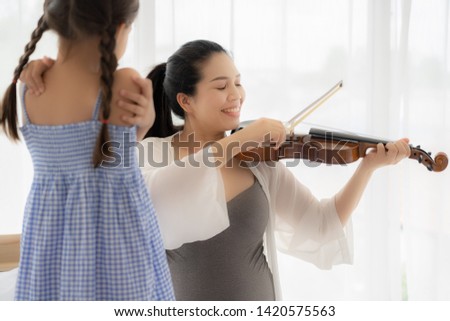 Mom plays violin for her daughter to listen.
