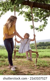 Mom Pushing Daughter On A Swing Set