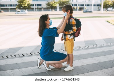 Mom Puts A Child A Mask And Escorts To School Or Kindergarten. A Boy With A Masked Backpack During A Coronavirus.