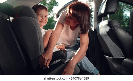 Mom puts her Kid son in car seat, safe car. Happy family. Mother secures her son in car seat using child safety belt. Family road trip. Mom cares about her sons safety. Child sits in car child seat