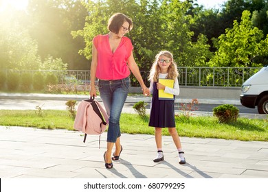 Mom And Schoolgirl Of Primary School Holding Hands. The Parent Takes The Child To School. Outdoors, Return To The Concept Of The School