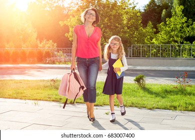 Mom And Schoolgirl Of Primary School Holding Hands. The Parent Takes The Child To School. Outdoors, Return To The Concept Of The School